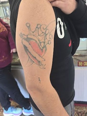 Tattoo of a crowned heart with a banner on a person's upper arm.