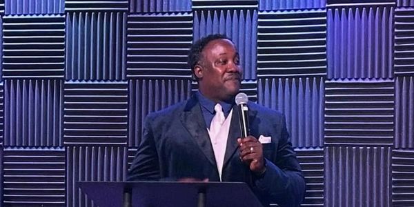 Man in suit speaking on stage with microphone.