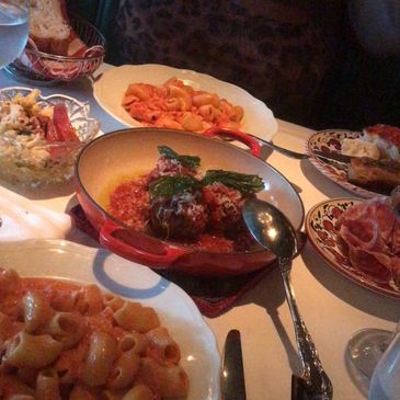 Italian meal with pasta, meatballs, and antipasto on a restaurant table.