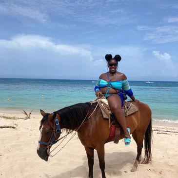 Woman in blue swimsuit sitting on a brown horse on a sandy beach.