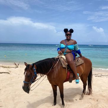 Woman in blue swimsuit sitting on a brown horse on a sandy beach.
