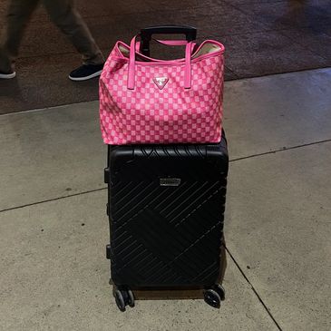 Pink patterned bag on a black wheeled suitcase.