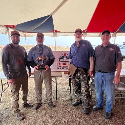 Four men standing under a tent, one holding a trophy.