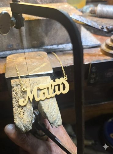 A gold necklace with the name "Malta" being crafted.