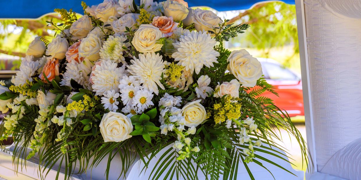 Funeral casket flower spray with white, pink, and greens on an open white casket. 