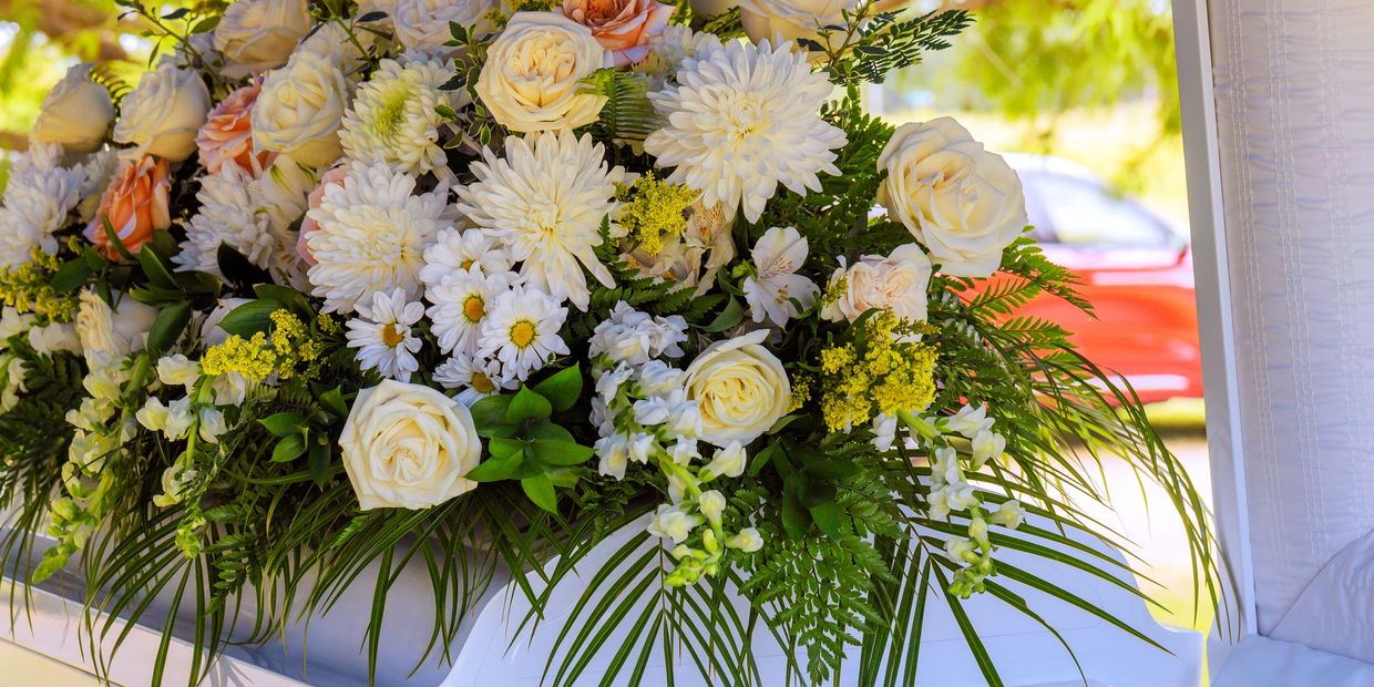 Funeral casket flower spray with white, pink, and greens on an open white casket. 