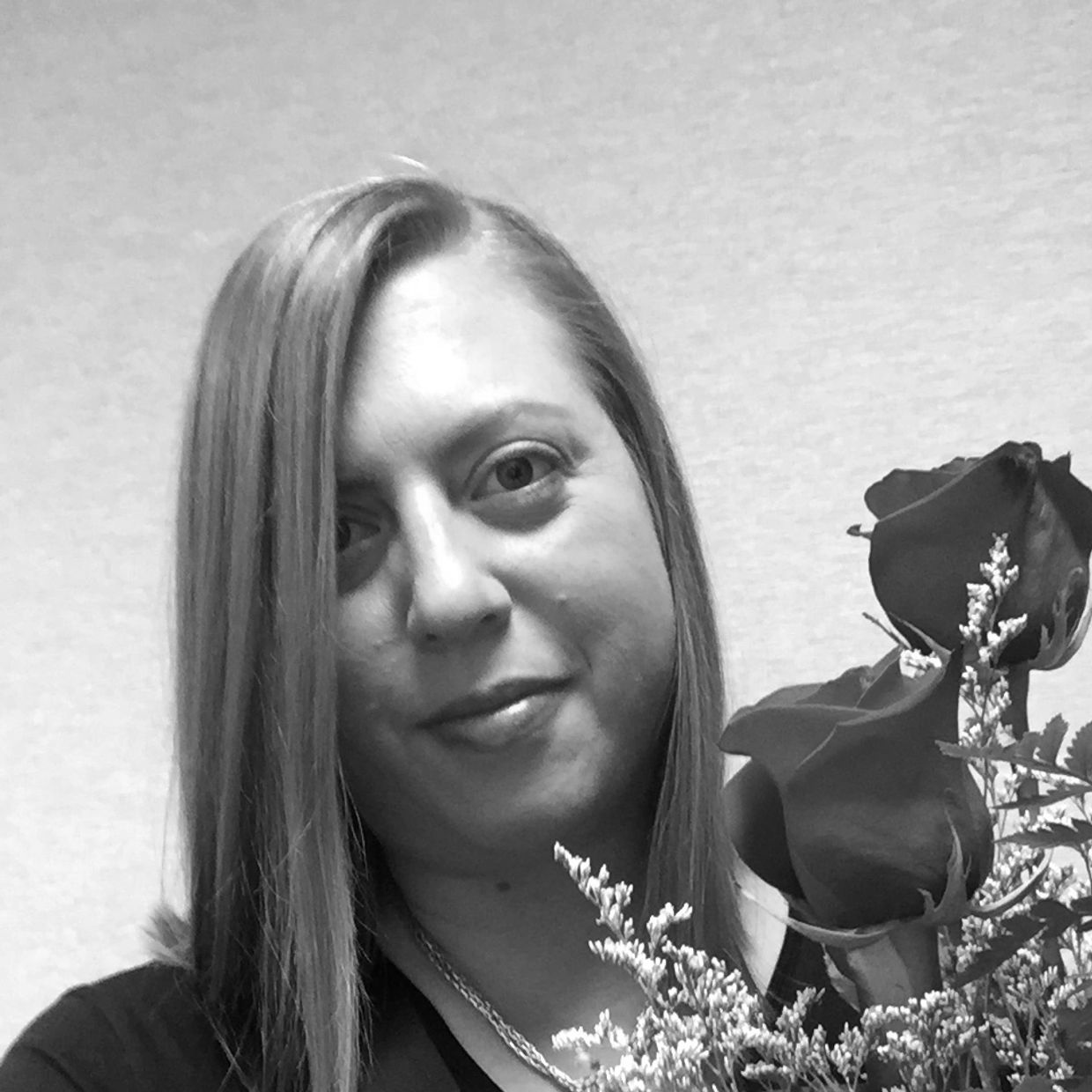 Black & white image of artist, Lauren, with shoulder-length hair & holding a bouquet of flowers. 