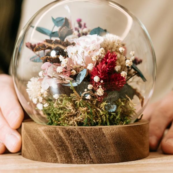 Close up of a globe cloche with real dried flowers and moss on a chunky wood base. 