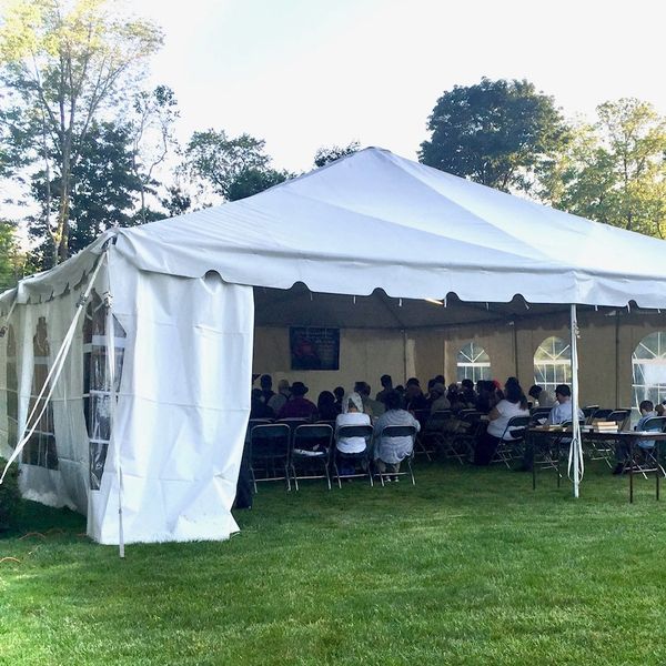Large white event tent with people seated inside on chairs.