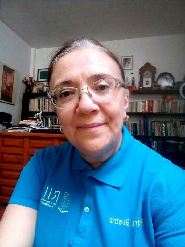 Mujer con gafas y camisa azul sonriente en una habitación con estanterías.