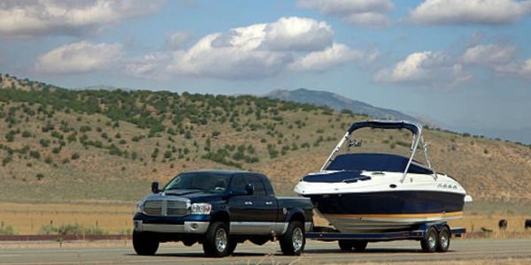 A black truck towing a boat on a trailer in a rural area.