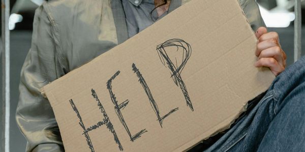 Person holding a cardboard sign with 'HELP' written on it.