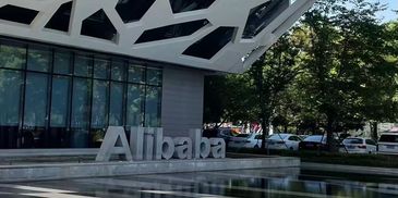 Alibaba sign outside a modern office building with trees and cars nearby.
