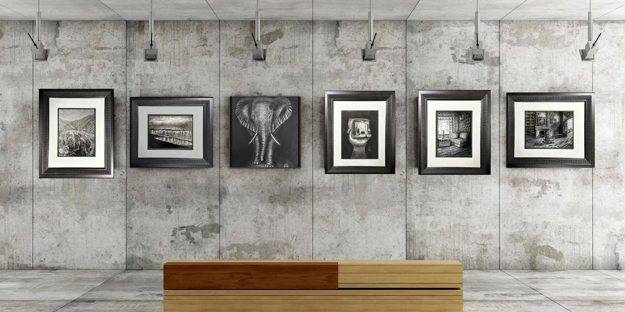 Gallery wall with black-and-white framed artworks, including an elephant and various scenes, on a concrete background.