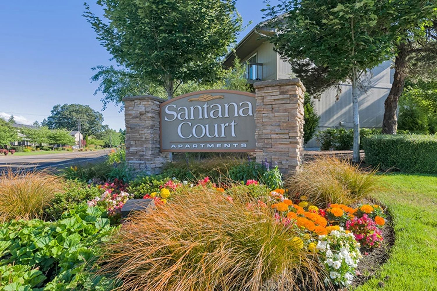 Stone sign for Santana Court Apartments surrounded by colorful flowers and greenery.