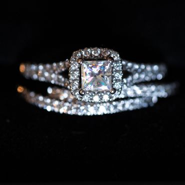 A sparkling diamond ring with a square-cut center stone on a dark background.