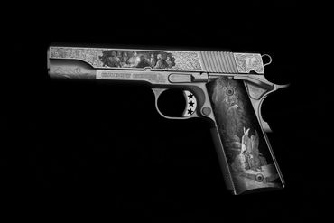 Intricately engraved silver handgun with detailed artwork on a black background.