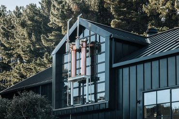 Modern black house with large glass windows and exposed pipes.
