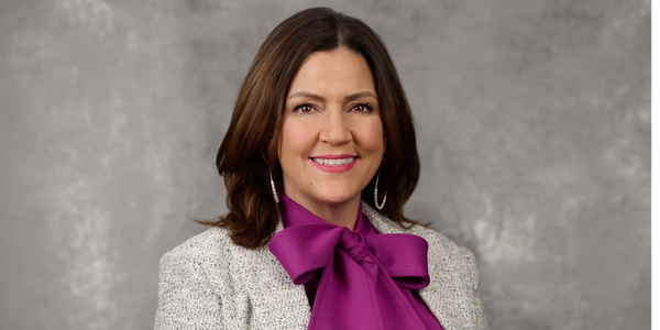 Professional woman smiling in a purple blouse with a bow and textured jacket.
