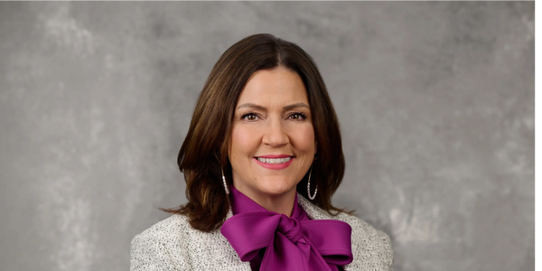 Professional woman smiling in a purple blouse with a bow and textured jacket.