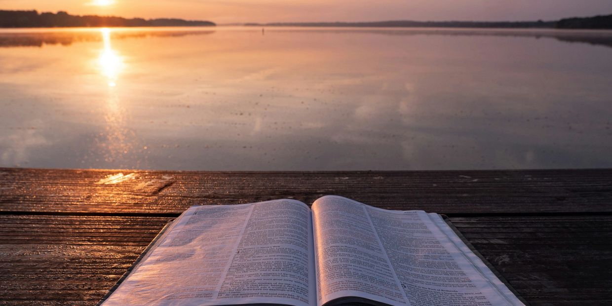 Christian Support - an open Bible on a table overlooking a peaceful sunset over the water.
