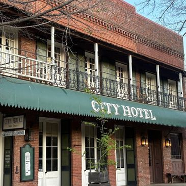 Front view of City Hotel with green awning and balcony.