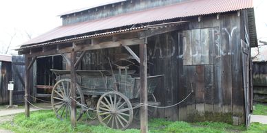 Old wooden wagon displayed outside a rustic barn.
