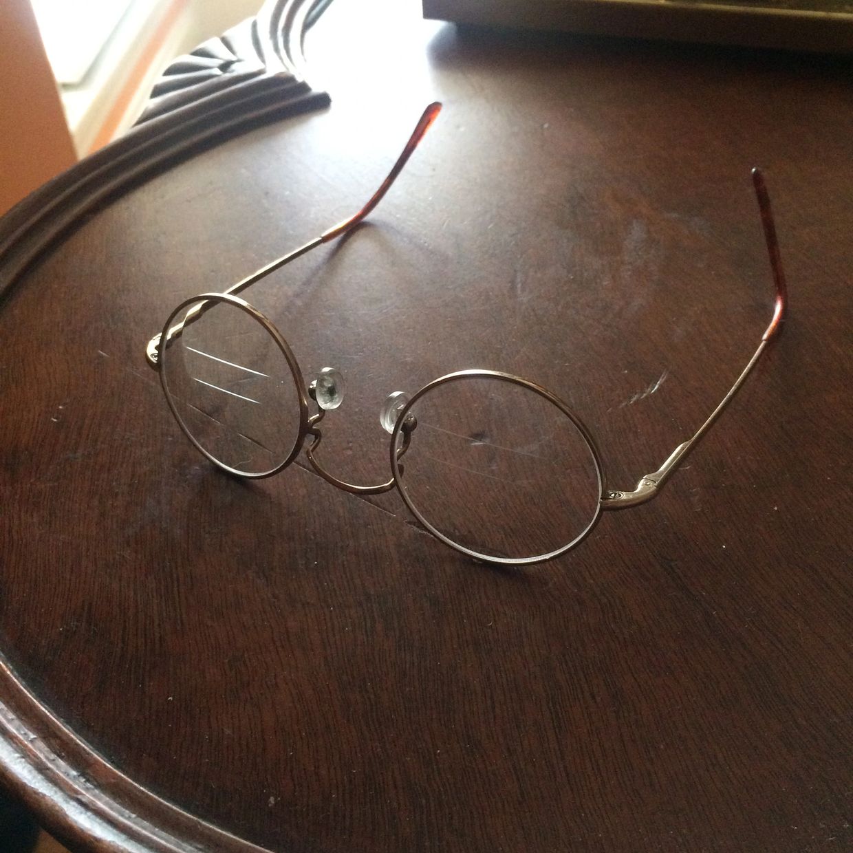 Round eyeglasses with thin metal frames resting on a wooden surface.