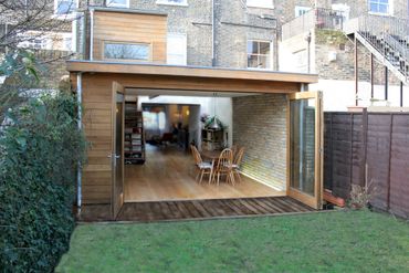 Modern backyard extension with large folding glass doors and wooden flooring.