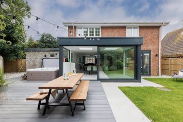 Modern backyard with patio, picnic table, and glass extension on house.