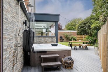 Outdoor patio with a hot tub and shower under a glass roof.