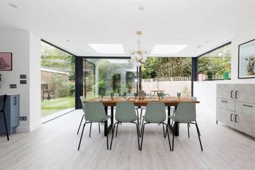 Modern dining room with glass walls overlooking a garden.