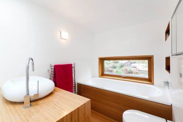 Modern bathroom with wooden accents and a large bathtub under a window.
