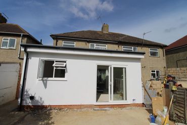 Newly built white extension at the back of a house with sliding doors.