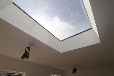 Two workers installing or repairing a large skylight from the ceiling inside a building.