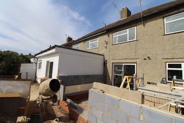 House extension under construction with brickwork and cement mixer.