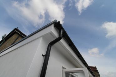 Close-up of a house corner with black gutters against a partly cloudy sky.