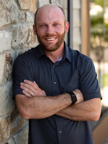 Smiling man leaning against a stone wall.