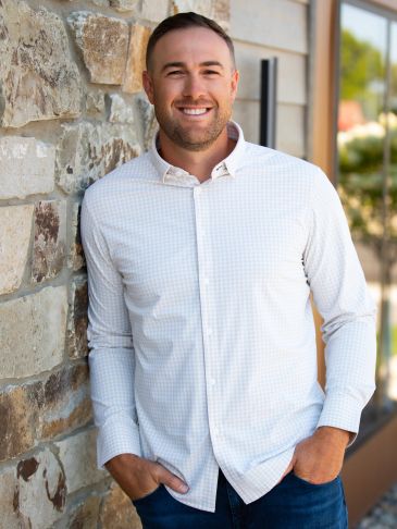 Smiling man in white shirt leaning against a stone wall.