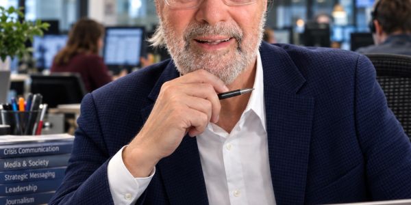Older man in a blue blazer holding a pen, smiling.