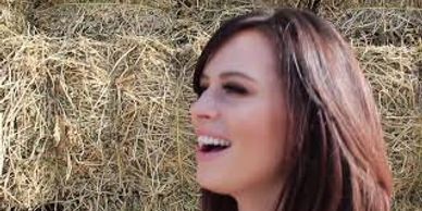 A woman with long brown hair laughing in front of hay.