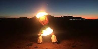 Two performers manipulate fire at sunset in a desert setting.