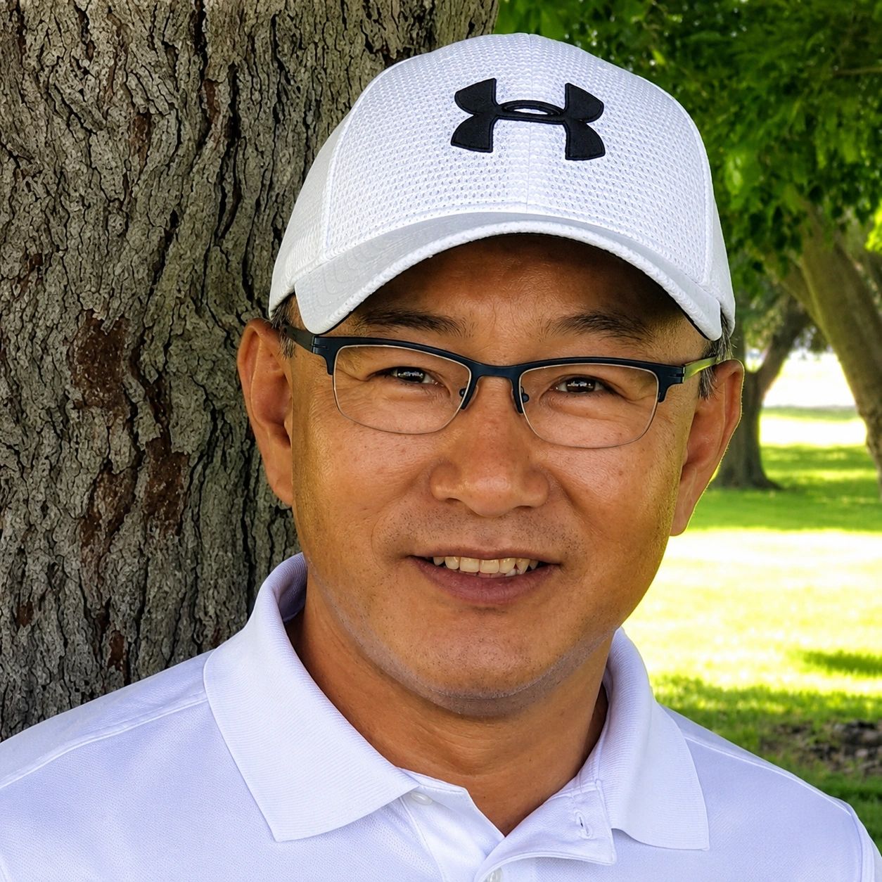 Smiling man wearing a white Under Armour cap and glasses.