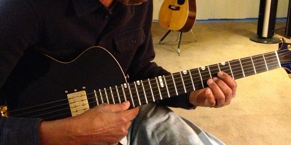Roger Boykin in his living room playing guitar and teaching the youth. 
