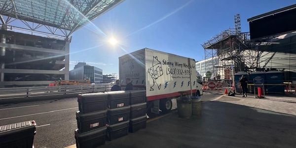 Delivery truck and stacked containers under a large glass roof in an urban area.