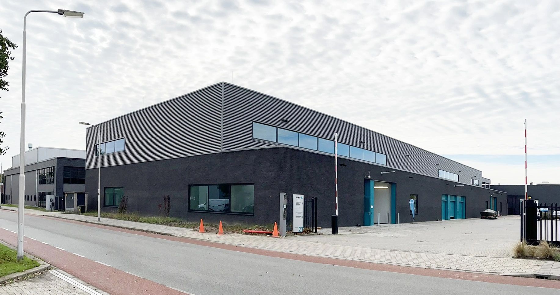 Modern industrieel gebouw met grijze gevel en blauwe deuren.