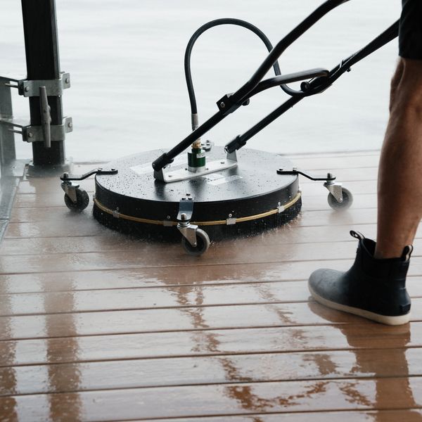 A person cleaning a wooden deck with a surface cleaner and water.