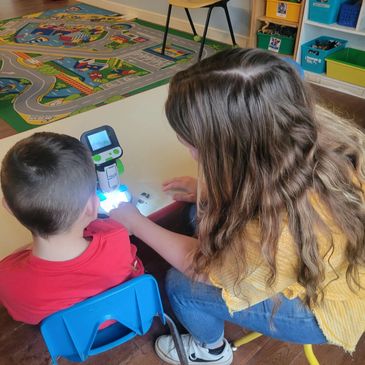 A woman helps a child with a small robot at a table in a classroom.