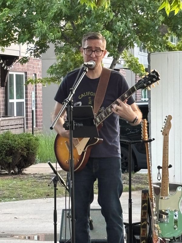 Man playing electric guitar and singing outdoors with equipment setup nearby.