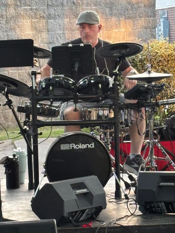A man playing an electronic Roland drum set outdoors.